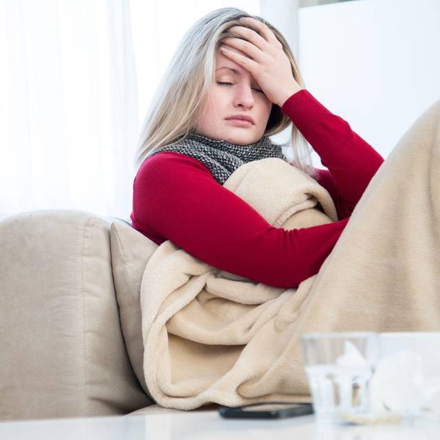 Eine Frau sitzt krank auf einem Sofa