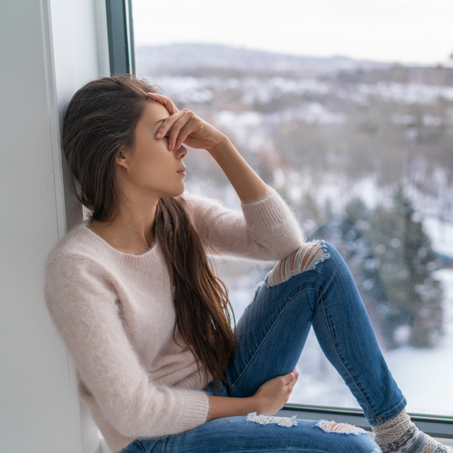 traurige Frau sitzt am Fenster und schaut in die kalte Winterlandschaft