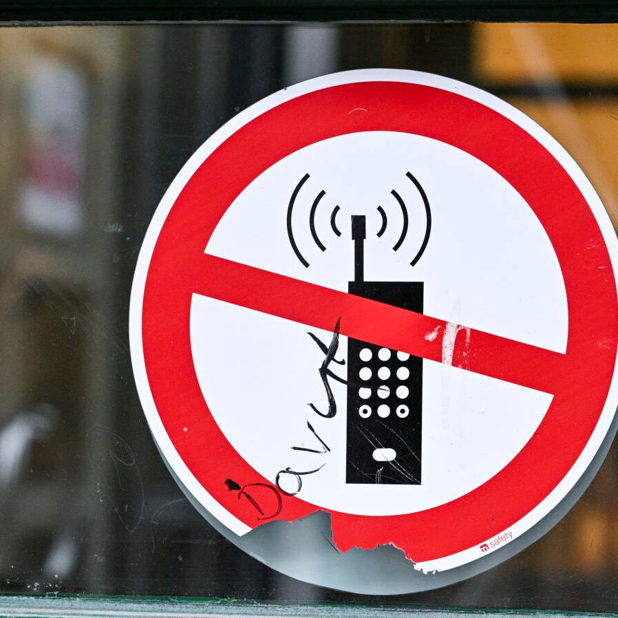 Ein Schild mit einem durchgestrichenen Handy-Symbol weist in einer Schule auf das Handyverbot hin.