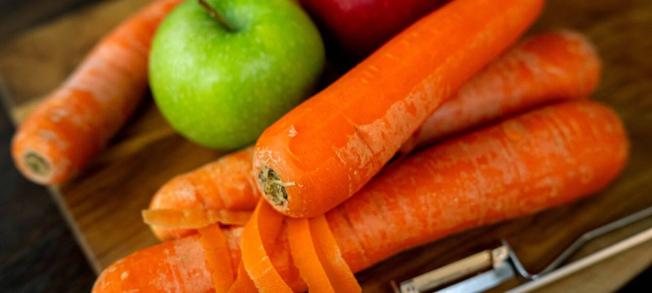 Auf dem Bild sind neben Karotten auch Äpfel auf einem Schneidebrett zu erkennen.